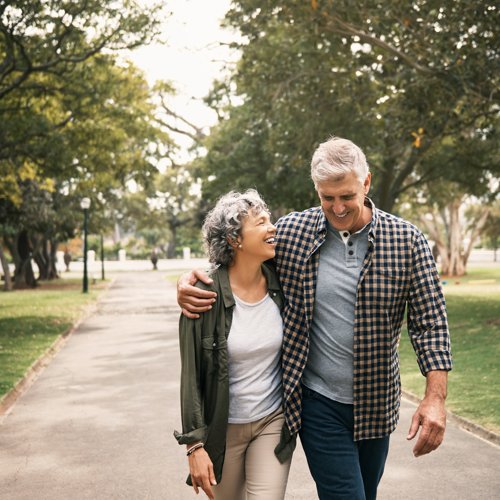 An older couple happily walking arm-in-arm down a park pathway.