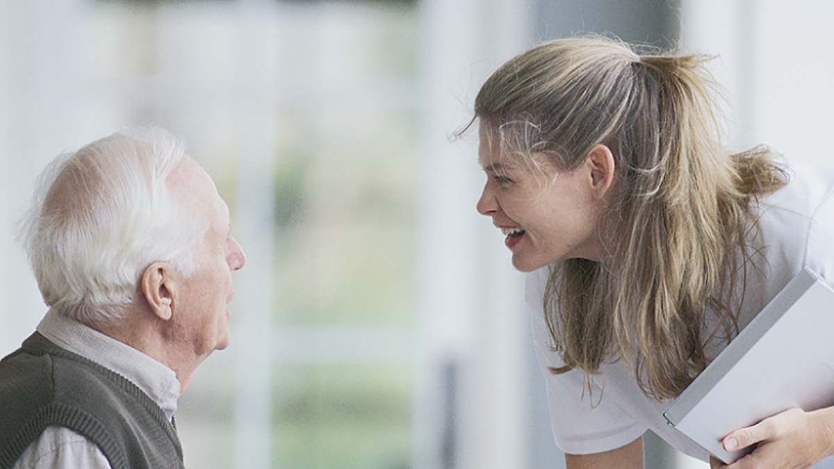 A caregiver smiling and engaging with an elderly man in a friendly and supportive manner. The image represents caregiving, senior care, or interaction between healthcare professionals and elderly patients.