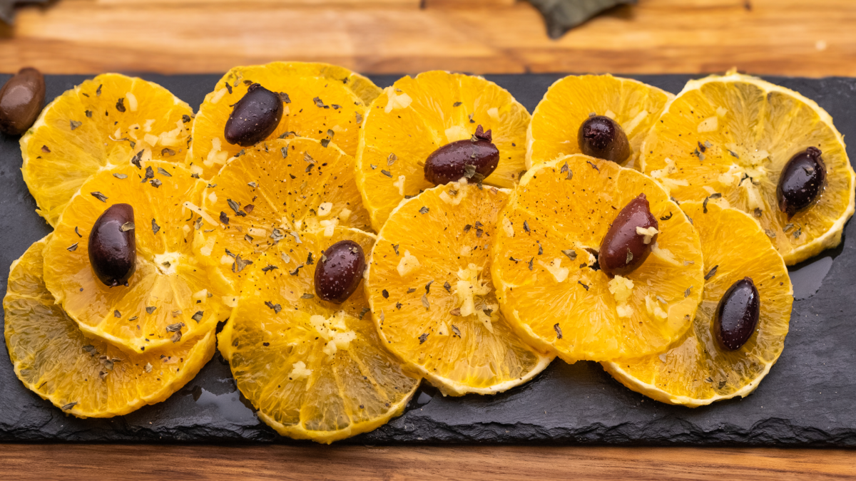 Sliced oranges arranged on a slate serving platter, garnished with olives and sprinkled with herbs.