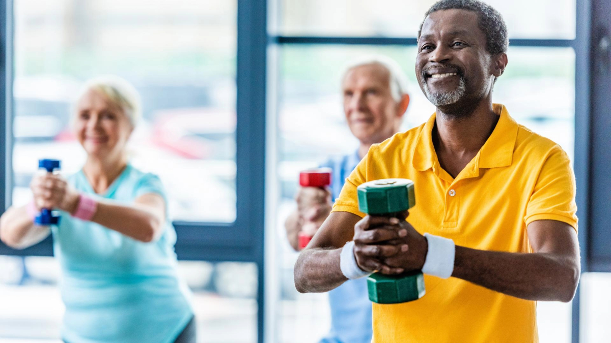 Three senior adults exercising with hand weights in a gym, smiling and focused on their workout.