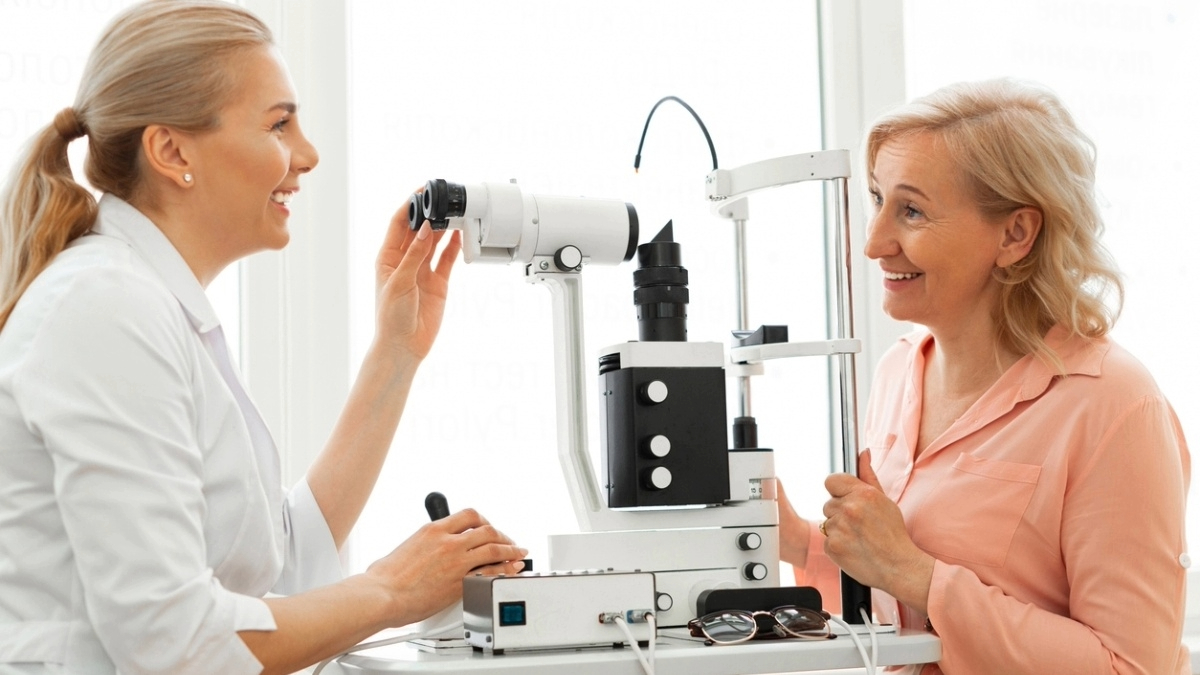 A person conducting an eye examination on another person using an ophthalmic machine in a bright clinical setting.