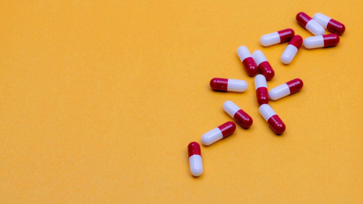 A group of red and white capsules scattered on a bright yellow background, with ample negative space to the left.