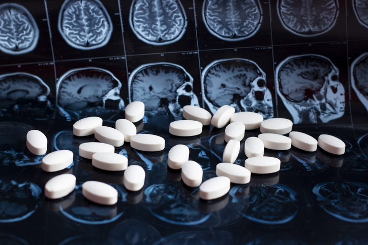 Pills on a table surrounded by brain scans. 