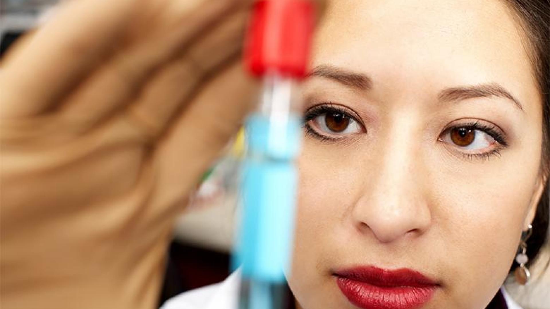 a close-up image of a woman's face and hand. She is looking at an out-of-focus vial.