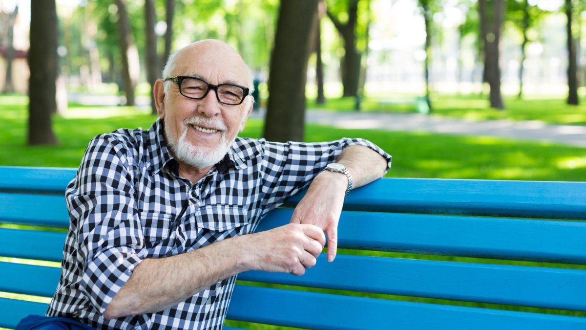 A smiling senior man sits on a blue park bench.