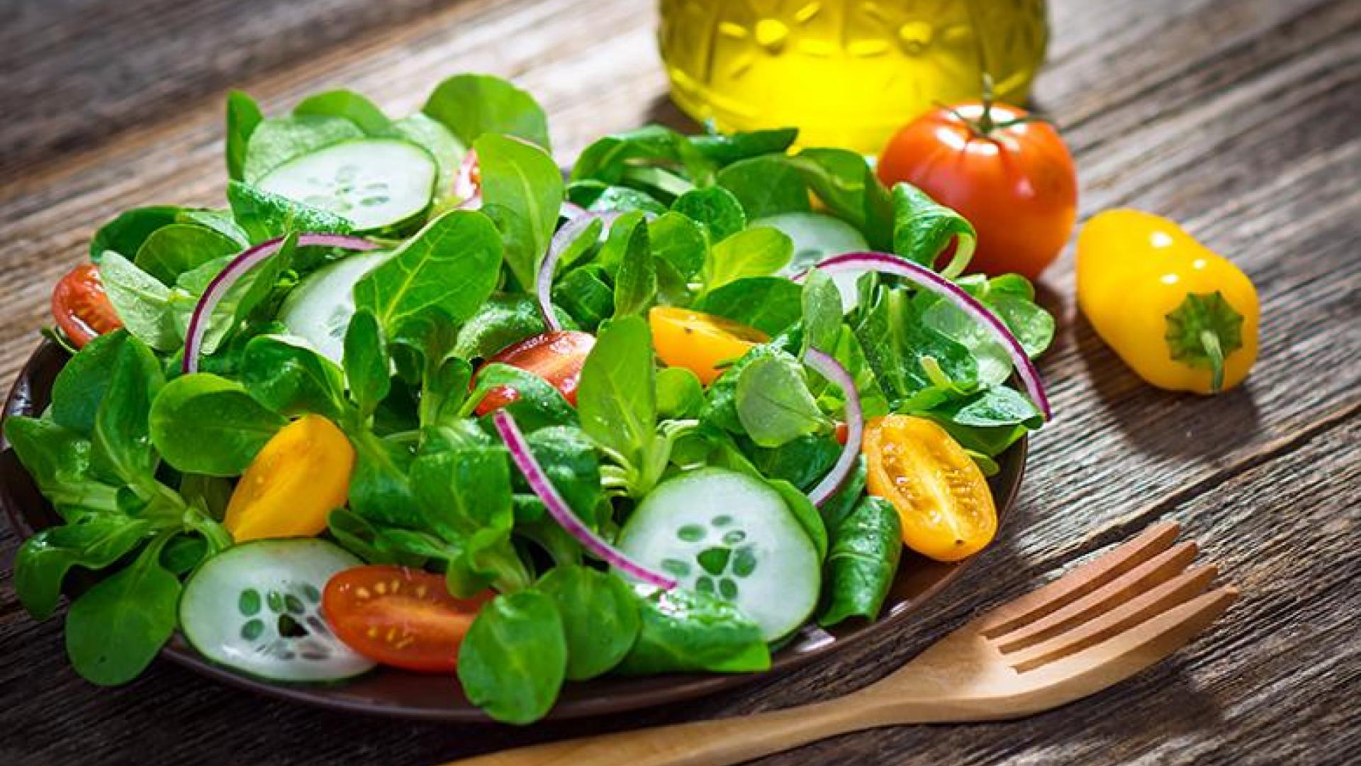 a fresh-looking, colorful salad on a wooden plate next to a wooden fork on a wooden table