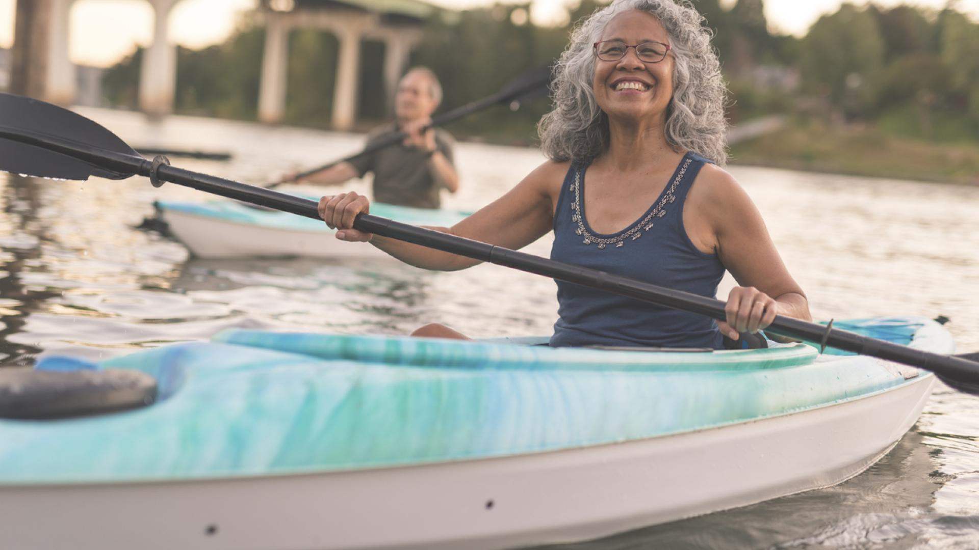 an older woman in a kayak smiles for the camera while holding her paddle aloft