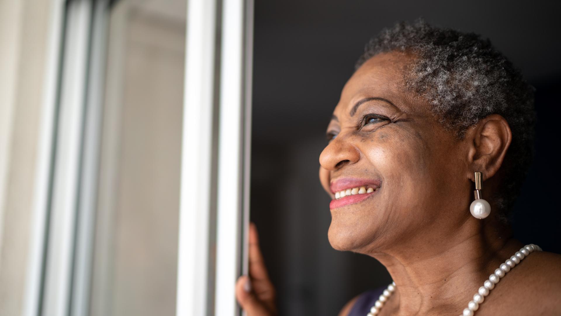 A smiling senior African American woman smiling while looking out the window.