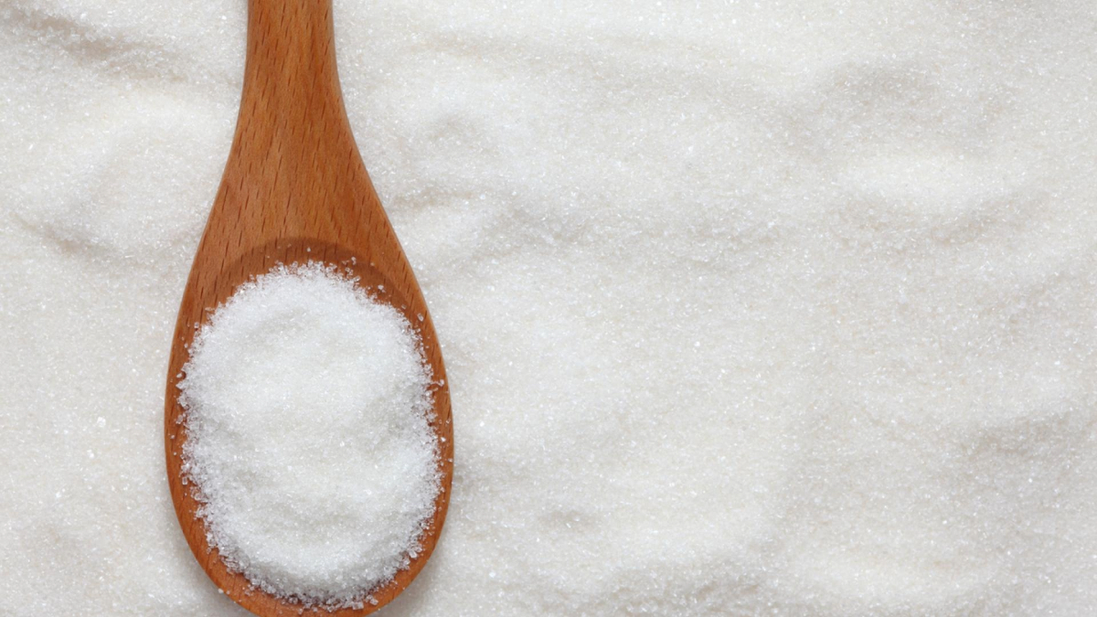 A wooden spoon filled with granulated sugar resting on a bed of sugar.