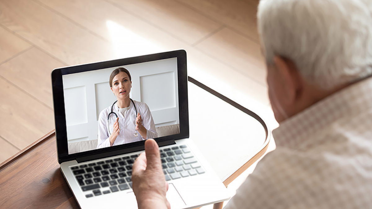 Person on a video call with a doctor, who is visible on the laptop screen, in a room with a white background.