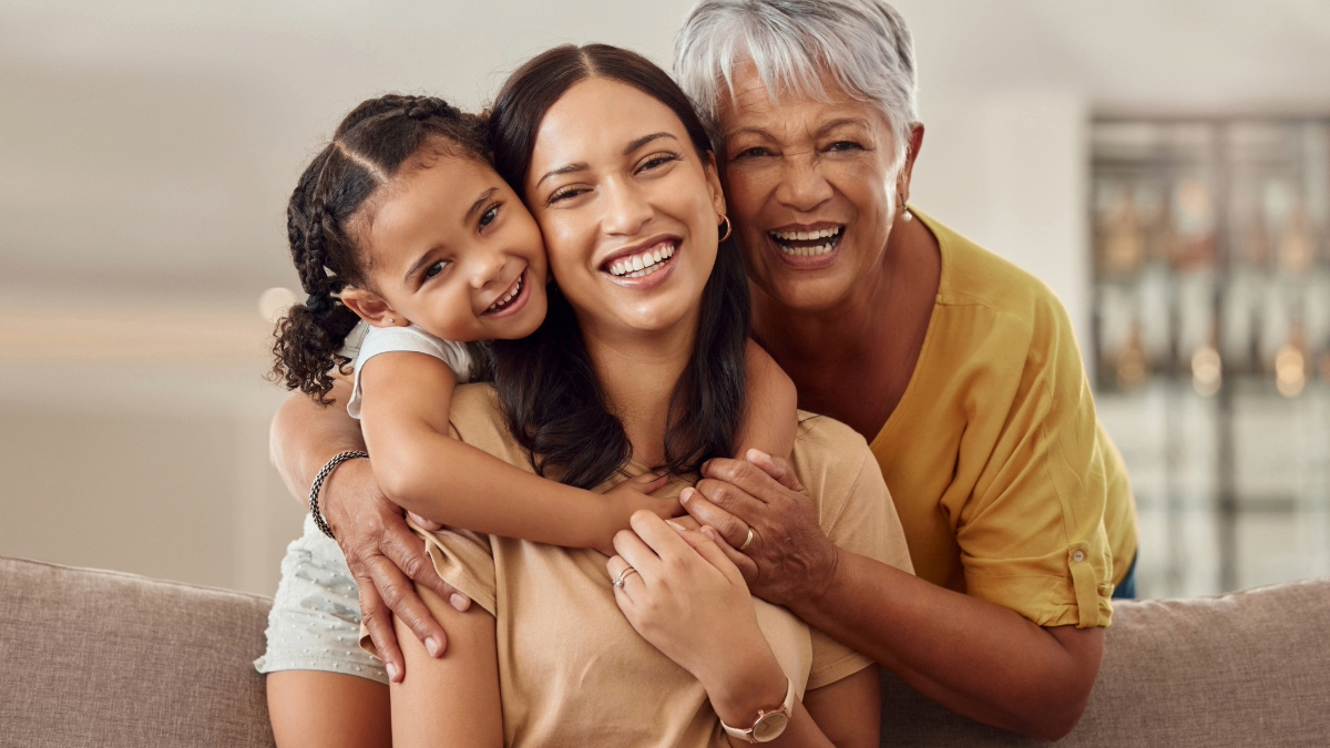 A joyful family moment featuring three generations embracing on a couch, with a child, an adult, and an elderly person smiling broadly.