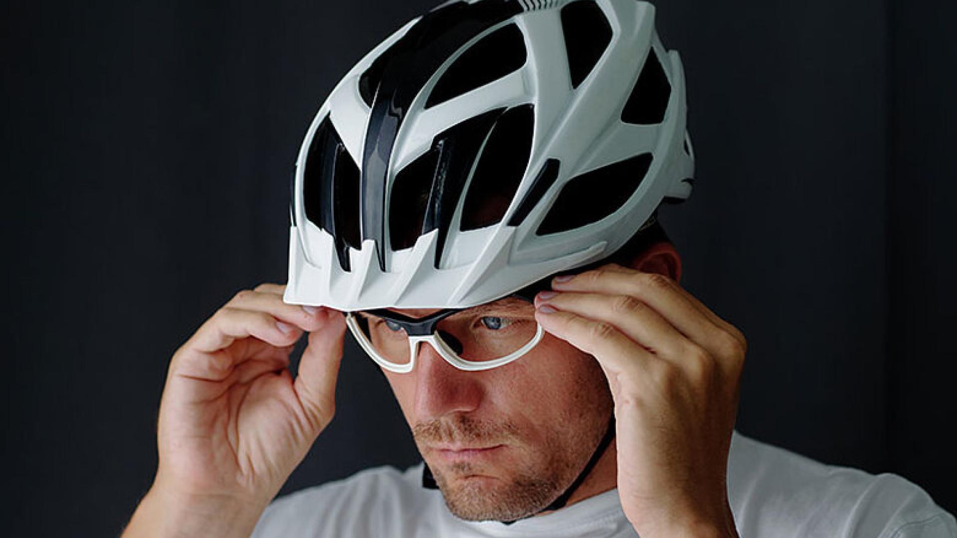 A man adjusting his white and black bicycle helmet while wearing sports glasses, focused and preparing for a ride.