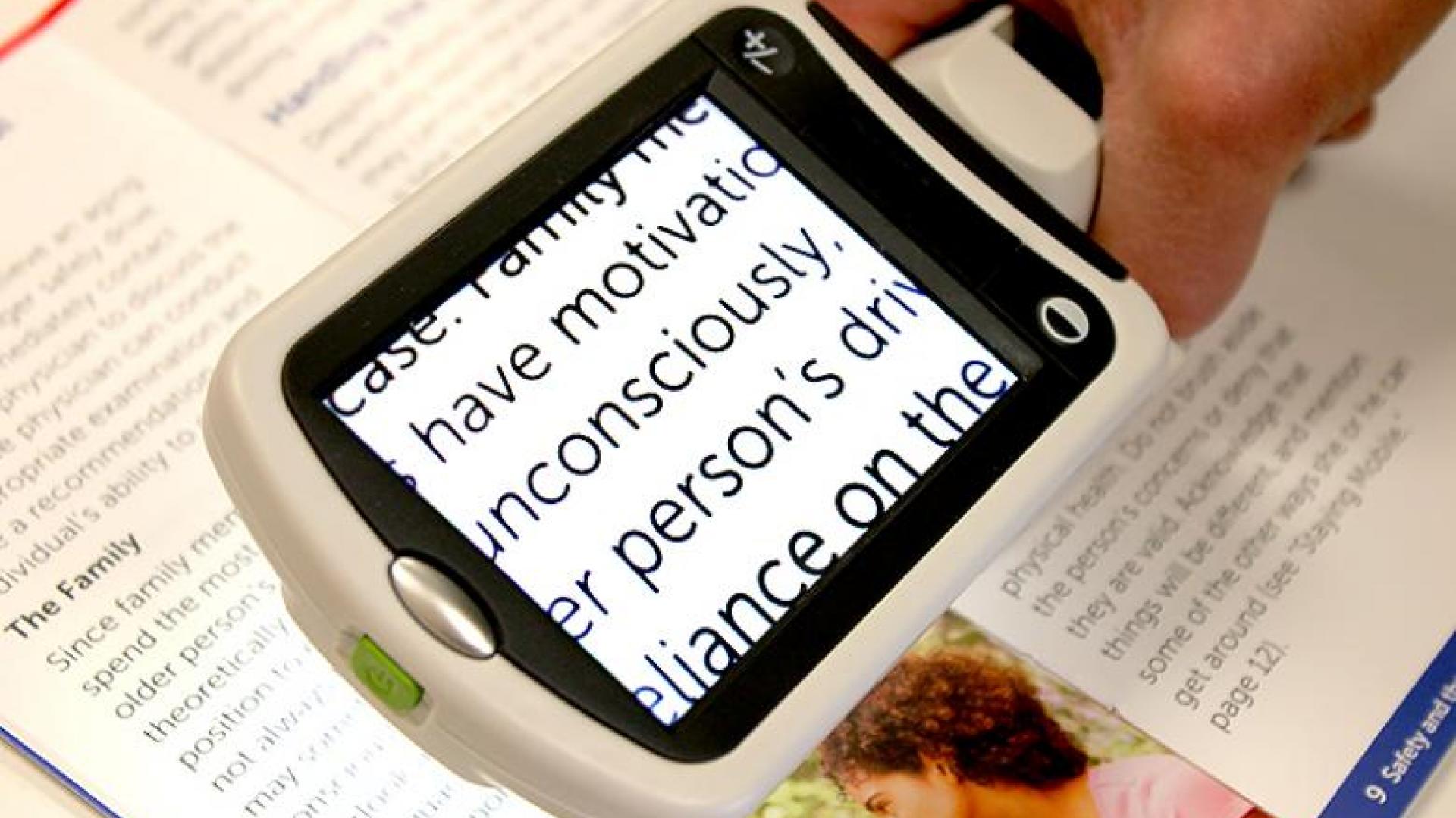 A person reading a brochure using a handheld video magnifier.