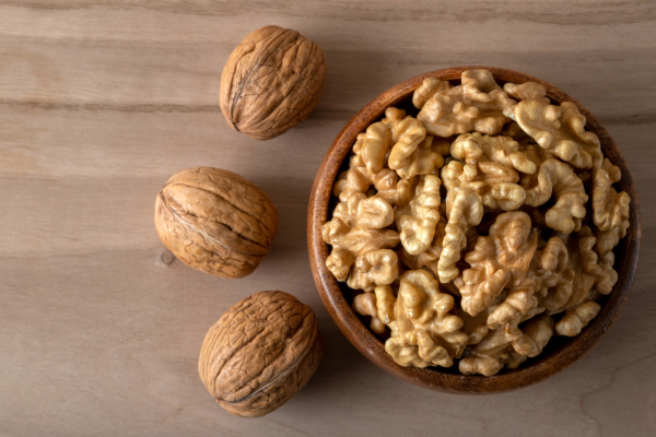 A bowl of shelled walnuts accompanied by whole walnuts on a wooden surface.