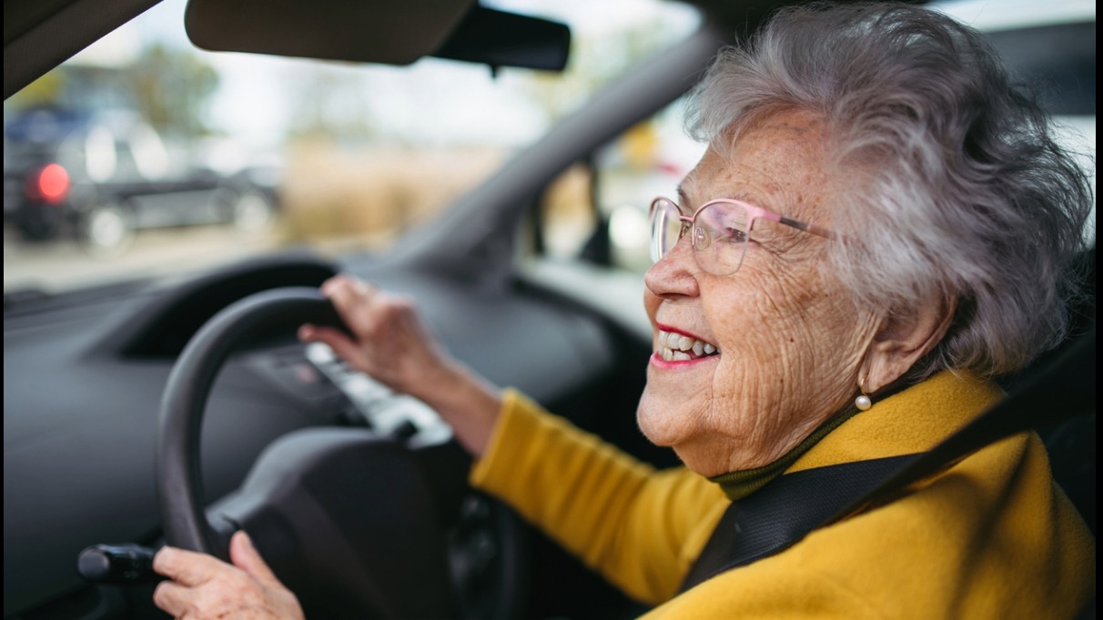 An elderly person smiling while driving a car.