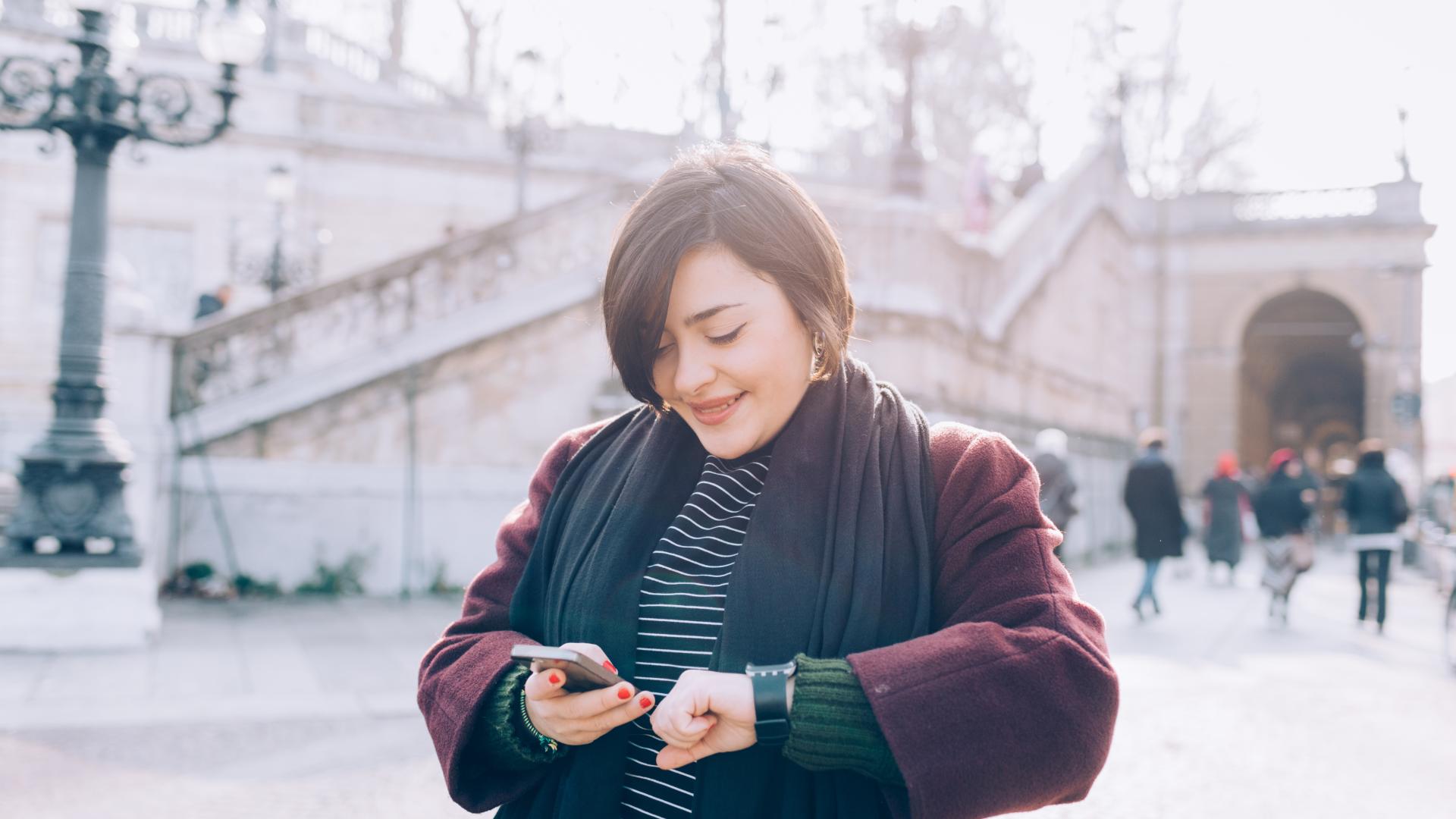 A woman wearing a smart watch device and looking at her mobile phone.