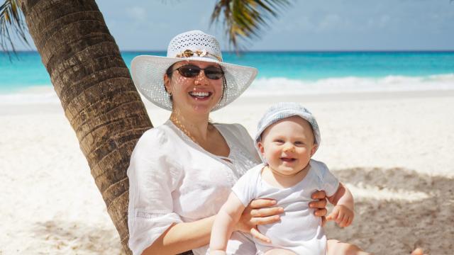 Woman and child smiling on a sunny beach. The woman is wearing a sun hat and sun glasses.