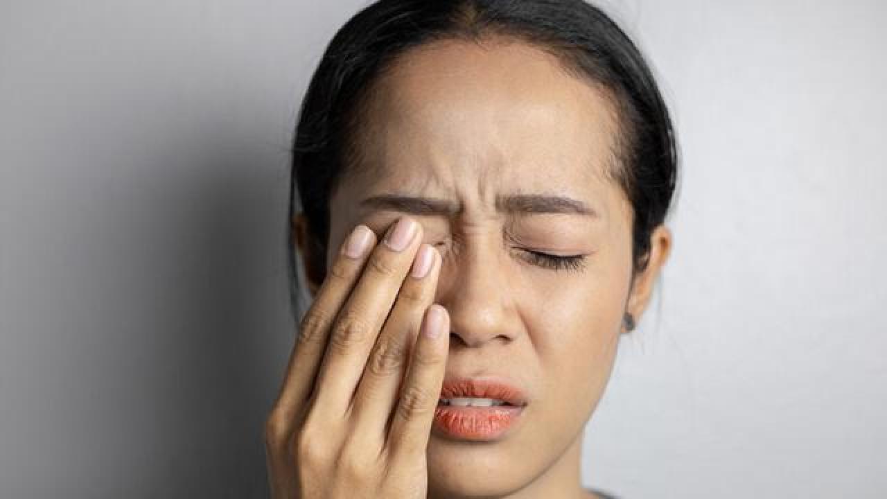 Person holding their eye in discomfort, showing signs of eye issues.