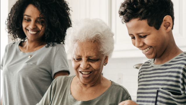 Three generations of a family cook and laugh together in a kitchen.