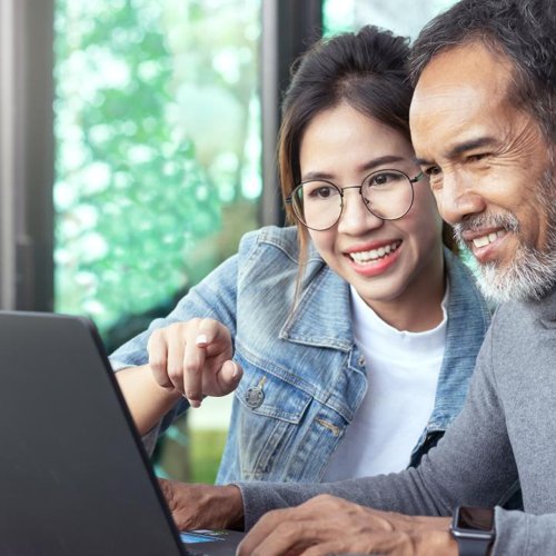 A granddaughter and grandfather look at a laptop screen.