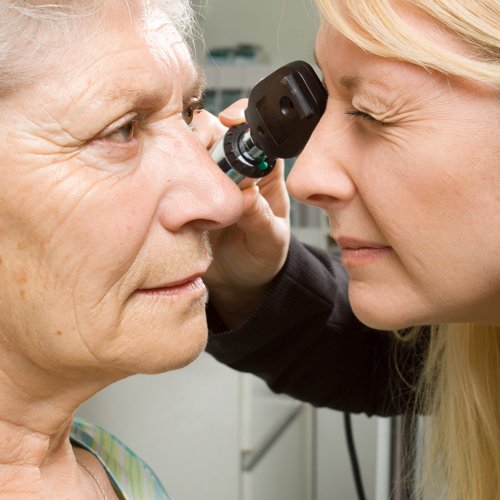 An eye doctor checks a senior woman's pupils.