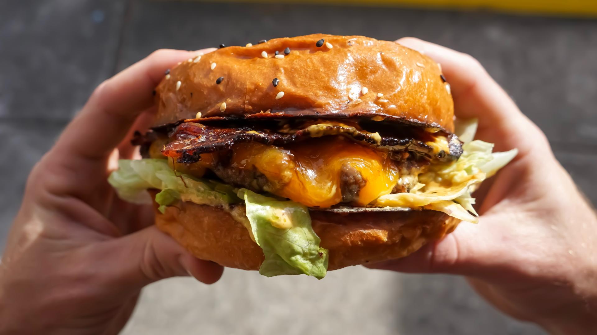 Hands holding a beef burger with cheese.