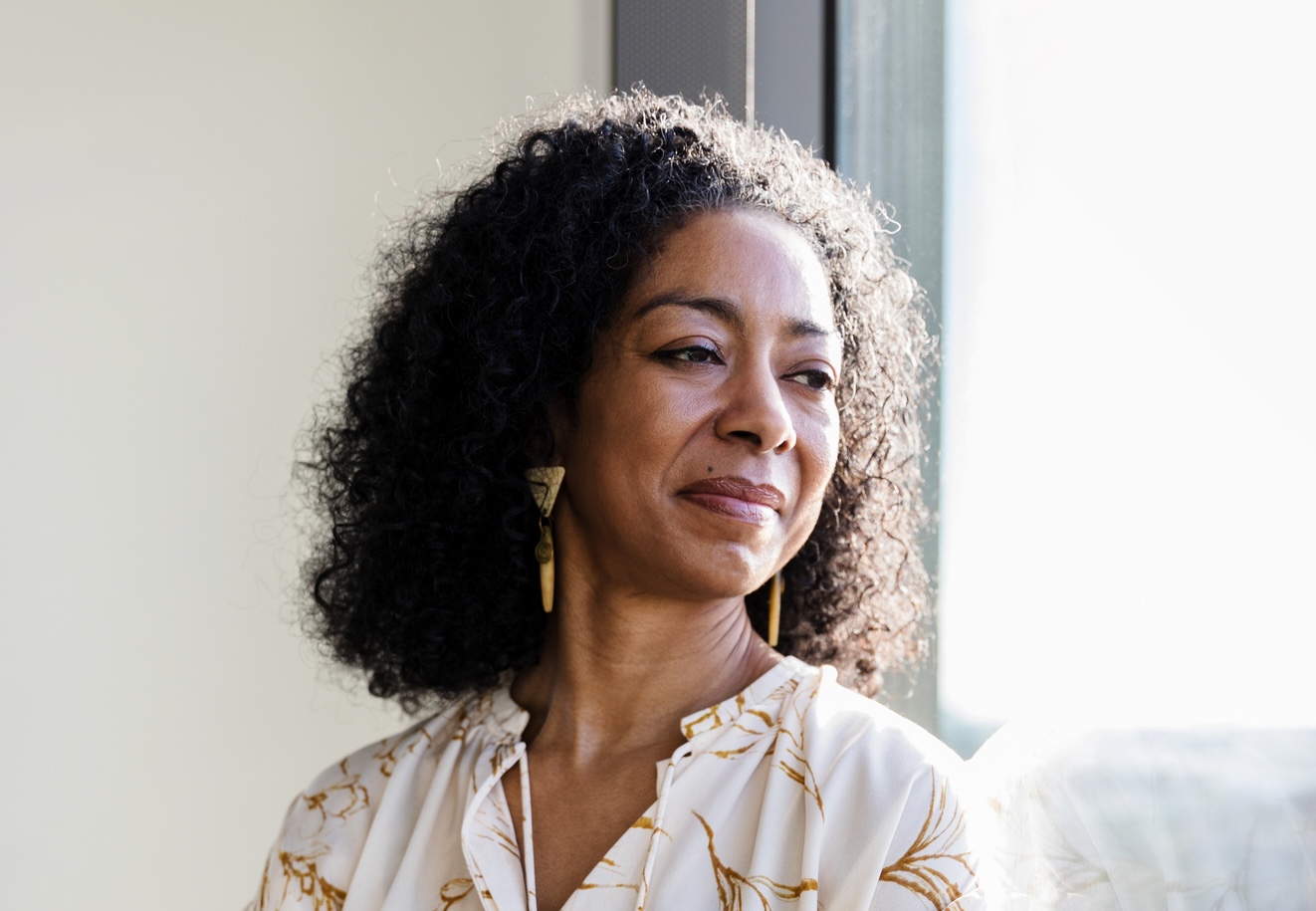 A mature African American businesswoman day dreams while looking out of her office window.