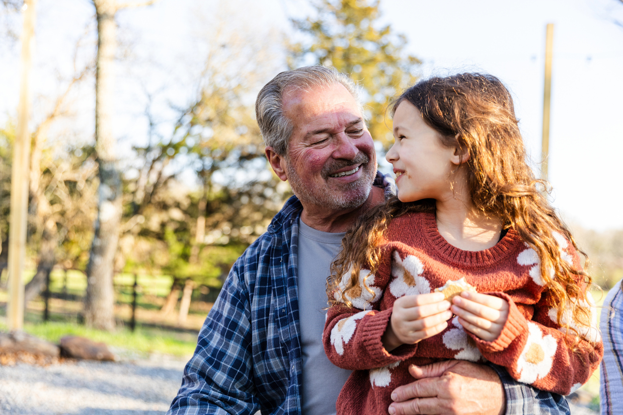 The elementary age girl looks back and smiles at her senior adult granddad as they enjoy their time outdoors.