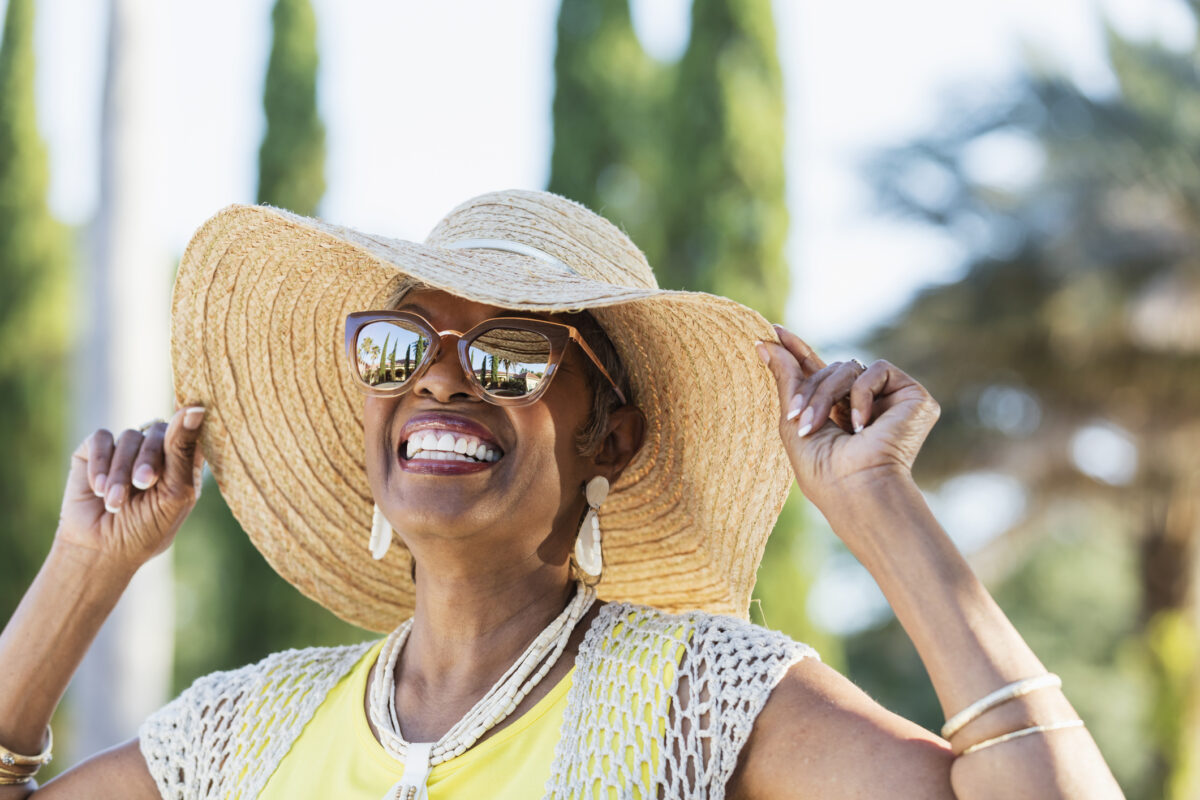 A woman looks joyful in a wide-brimmed hat and sunglasses.