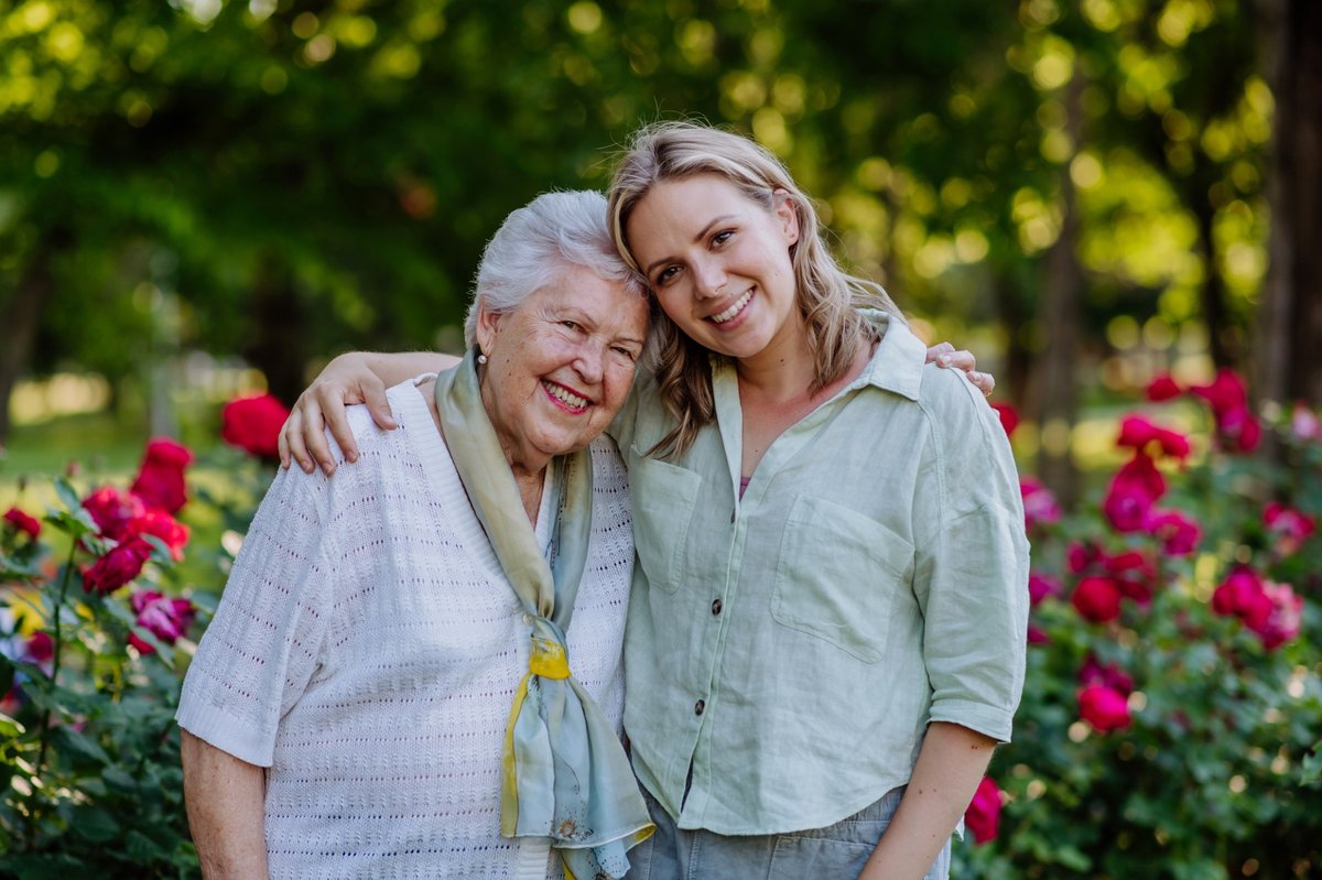 A grandmother and granddaughter smile together in the park.