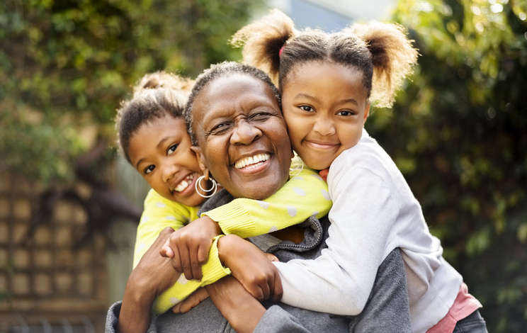 Senior woman cuddling her two granddaughters outdoors.