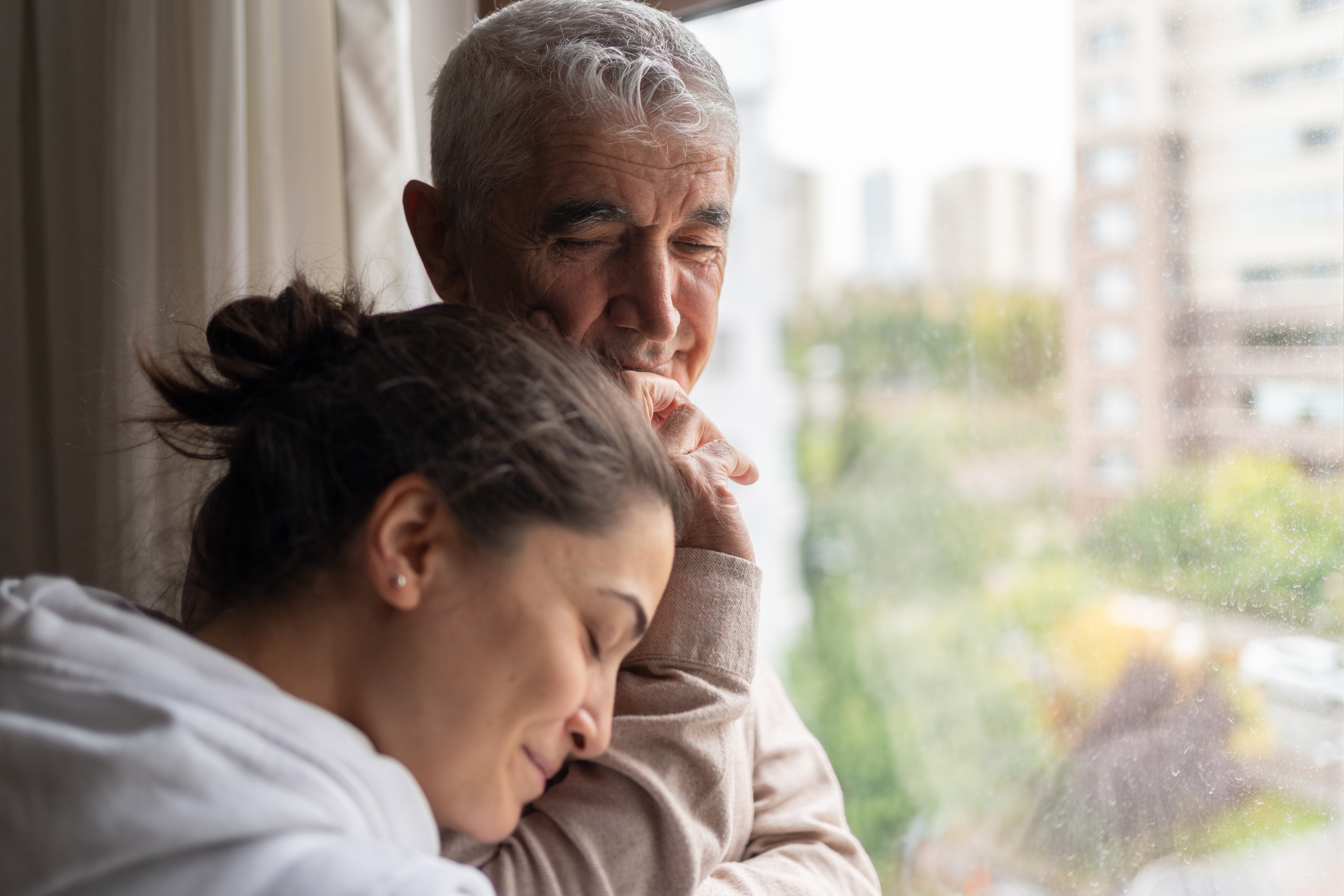 Daughter Embracing Her Contemplative Senior Father At Home