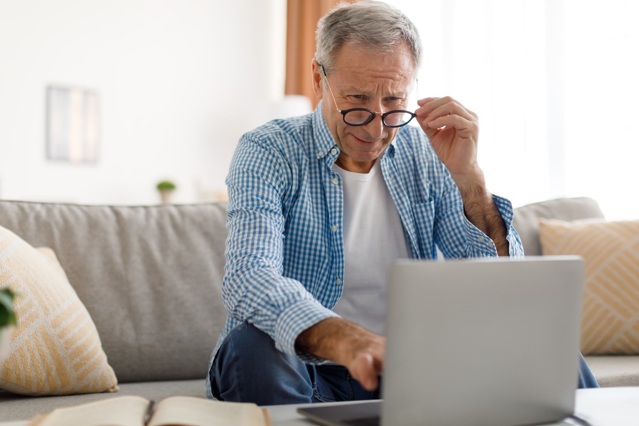 Mature man squinting using laptop, looking at screen.